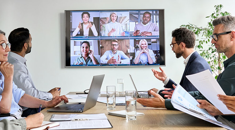 Diverse employees on online conference video call on tv screen in meeting room.